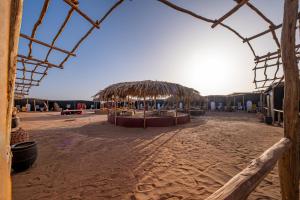 a beach with a straw umbrella and chairs on it at Les voix de Sahara Lodge in Mhamid