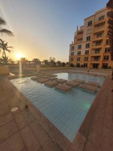 a swimming pool with benches in front of a building at Royal Beach Apartment in King Abdullah Economic City