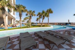 a swimming pool with benches and palm trees next to a building at The Oasis By Liquid Life in Orange Beach