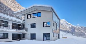 a white building with snowy mountains in the background at Apart Galeon in Pettneu am Arlberg