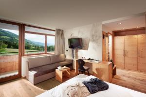 een hotelkamer met een bed, een bank en een televisie bij Naturhotel Die Waldruhe in Chienes