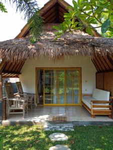 Casa con techo de paja, cama y sillas en Bintang Tiga Bungalows Gili Air en Gili Air