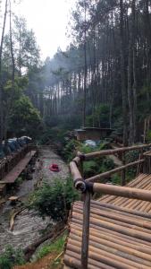 una valla de madera junto a un río con árboles en wulandari reverside camping ground pinus singkur en Bandung