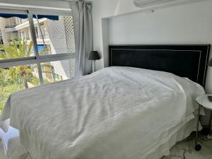 Cama blanca con cabecero negro y ventana en Skol Apartments Marbella, en Marbella