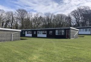 a black building with white doors and a grass field at Cosy Cabin - Bideford Bay Holiday Park in Bideford