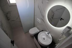 een badkamer met een wit toilet en een ronde spiegel bij Vila Ori in Ksamil