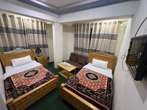 two beds in a room with a tv and a couch at Blue Sky Hotel & Restaurant in Skardu
