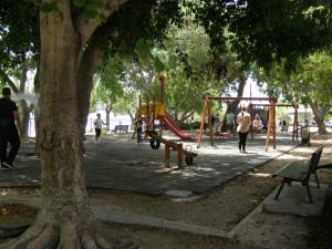 a park with a playground with people walking and a tree at Doll house next to the sea in Agioi Theodoroi