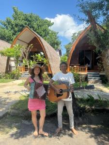 un hombre y una mujer parados frente a una casa con una guitarra en We'Be Cottages, en Gili Meno