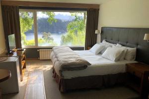 1 dormitorio con 1 cama grande y ventana grande en Puerto Manzano Suites by Visionnaire en Villa La Angostura