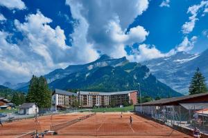 einen Tennisplatz vor einem Gebäude mit Bergen in der Unterkunft Eurotel Victoria Les Diablerets Superior in Les Diablerets