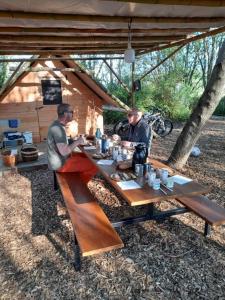 Dois homens sentados numa mesa de piquenique em frente a uma cabana. em Camp du Père Castor em Simard
