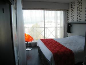 a bedroom with a bed and a window with a red chair at Hôtel Le Nautic in Arcachon