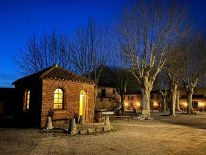 um pequeno edifício de tijolos com um banco e árvores à noite em Mas Sant Jordi em Alénya