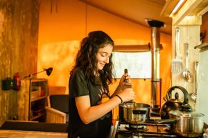 a woman standing in a kitchen preparing food in a pot at Luxury Safari Tent with Hot Tub in Ancient Woodland in Acton Scott