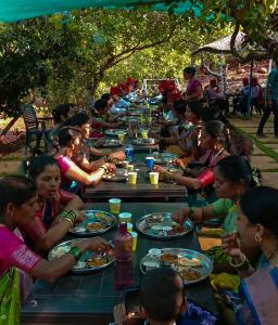 Chalobahills Farmstay Resort في Ajra: مجموعة من الناس يجلسون على طاولة طويلة يأكلون الطعام