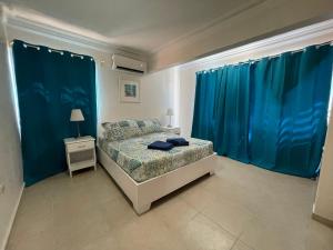 a bedroom with blue curtains and a bed and a nightstand at Karimar Beach Condo Hotel in Punta Cana