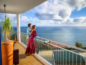 een man en vrouw op een balkon met uitzicht op de oceaan bij Indigo Star House in Ribeira Brava