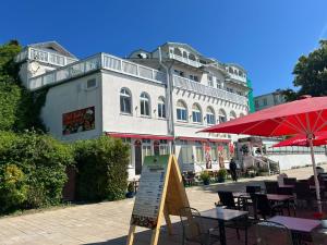 a white building with a red umbrella and tables and chairs at Fährblick - Pension direkt am Wasser in Sassnitz