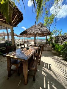 a wooden table with chairs and an umbrella on the beach at Bahari Beach Bungalows in Jambiani