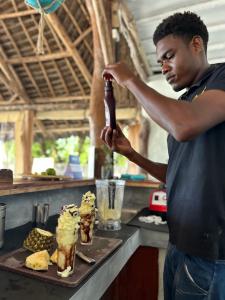 un homme tenant une bouteille devant deux cocktails dans l'établissement Bahari Beach Bungalows, à Jambiani