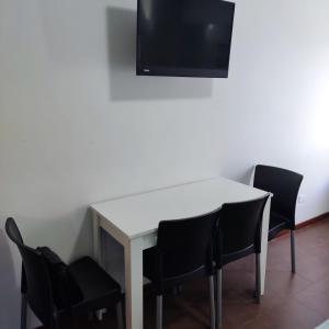 een witte tafel met zwarte stoelen en een tv aan de muur bij Buenos Aires Center Apart in Buenos Aires