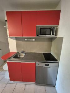 a kitchen with red cabinets and a sink and a microwave at Appartement Saint cyprien plage in Saint-Cyprien