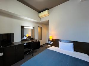 Hotel Route-Inn Fukui Ekimae في فوكوي: غرفة نوم بسرير ومكتب وتلفزيون