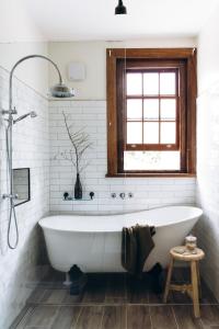 baño blanco con bañera y ventana en Gatekeepers Lodge - A Historic Hobart Experience, en Hobart