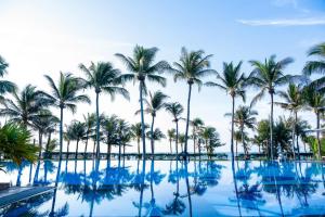 a pool with palm trees and the ocean at Sunny Beach Resort & Spa in Mui Ne