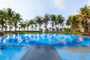 a large swimming pool with palm trees in the background at Sunny Beach Resort & Spa in Mui Ne