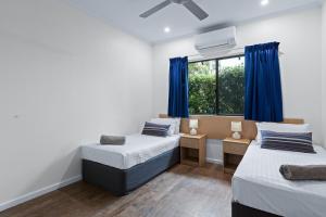 two beds in a room with blue curtains and a window at Cable Beachside Apartments in Broome