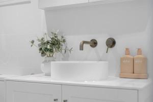 a white kitchen with a sink and a vase with two bottles at Toowoon Bay - Tranquil Couples Retreat - EV Powerpoint in Long Jetty +20 photos