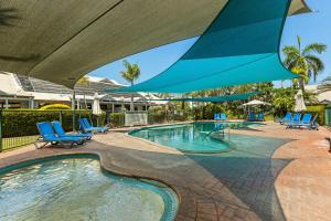 a swimming pool with blue chairs and a large umbrella at Cable Beachside Apartments in Broome