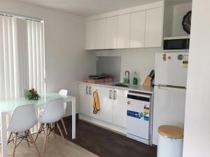 a kitchen with white cabinets and a table and a refrigerator at West Auckland Delight Stay in Auckland