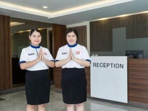 two women are standing with their hands in front of a sign at B2 Korat Premier Hotel in Ban Liap