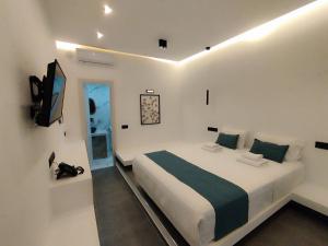a white bedroom with a bed and a television at Rigas Hotel Skopelos in Skopelos Town
