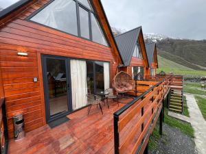a house with a wooden deck with a chair on it at Cozy Home Kazbegi in Stepantsminda