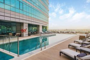 Hilton Bahrain في المنامة: مسبح الفندق مع كراسي الصالة والمبنى