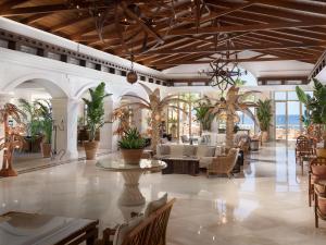 eine Lobby mit Tischen, Stühlen und Palmen in der Unterkunft Grecotel Marine Palace & Aqua Park in Panormos