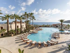 a swimming pool with chaise lounges and chairs and the ocean at Grecotel Marine Palace & Aqua Park in Panormos Rethymno