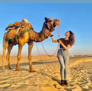 a woman standing next to a camel in the desert at Desert Safari Jaisalmer in Sām