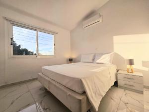 um quarto branco com uma cama grande e uma janela em 2BD Garden Apartment em Pafos