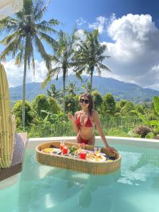 une femme en bikini assise dans une piscine avec un plateau de nourriture dans l'établissement Gladak di Uma Bali, à Sidemen