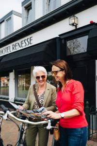 Duas mulheres estão ao lado de uma bicicleta. em Hotel Renesse em Renesse