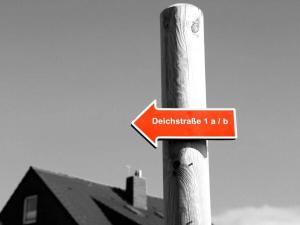 a red sign on a wooden pole with a house at House in Legde "East" in Norderney