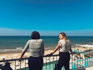 Dos mujeres de pie en un balcón con vistas a la playa en Hotel La Battigia, en Alcamo Marina