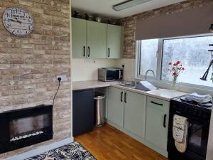 a kitchen with white cabinets and a brick wall at Little Haven Chalet Withernsea in Withernsea