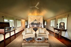 a bedroom with a bed and a couch and chairs at Gorah Elephant Camp in Addo