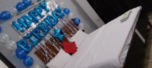 a birthday cake with blue balloons on a table at Hotel The Royal Stay in Noida